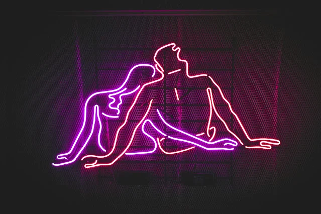 Neon pink outline of a couple sitting back to back in a moody, intimate setting