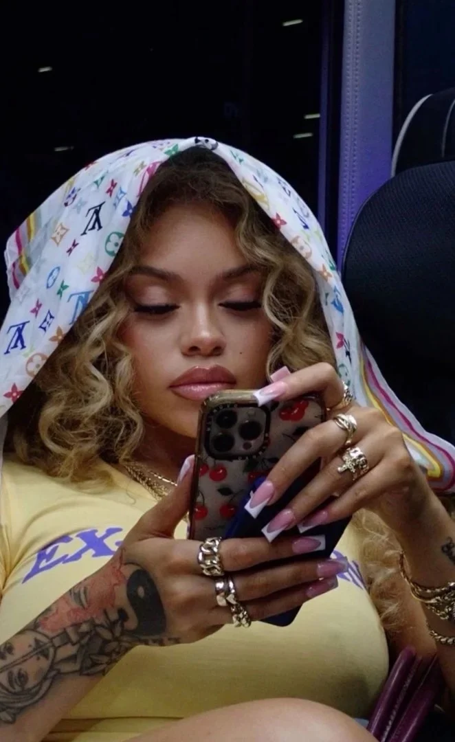 Confident woman with soft glam and long nails texting on her phone, representing feminine energy, soft life mindset, and how to ask a man for money in dating.