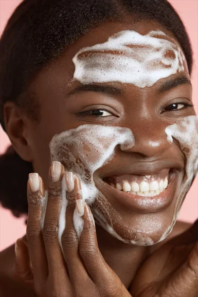 Black woman smiling while cleansing her face with foaming skincare